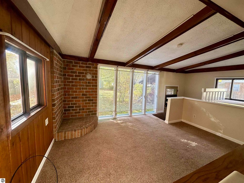 Bright interior of a home at 209 W Fifteenth Street, Traverse City, featuring a cozy living area with brick accents, large windows, and a view of the backyard, highlighting its potential as a second bedroom or family room.