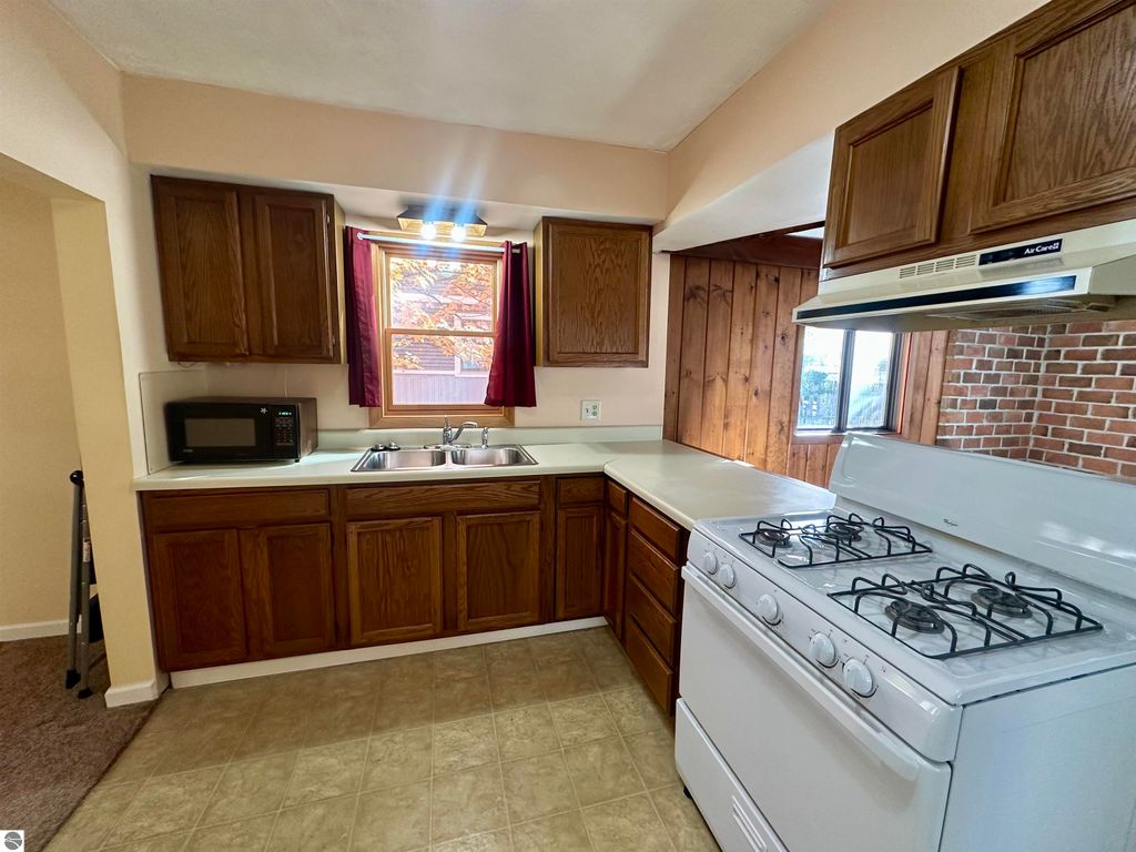 Kitchen with wooden cabinets, white gas stove, double sink, and window, featuring a cozy and bright atmosphere in the Traverse City home for sale at 209 W Fifteenth Street.