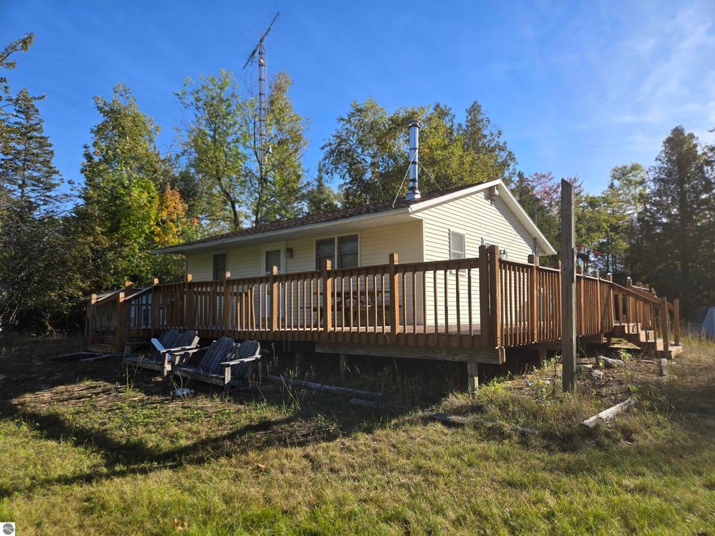 Cozy 2-bedroom, 1-bathroom home with large wrap-around deck on wooded 25.21-acre lot in Harrisville, MI, surrounded by trees and nature.