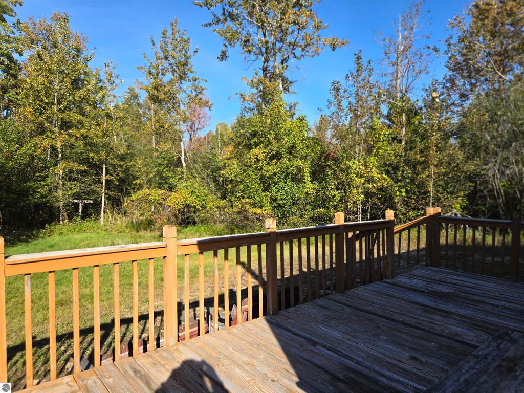 Wooden deck overlooking a wooded area with trees and blue sky, highlighting the serene outdoor setting of the 2-bedroom home at 5971 E Point Road, Harrisville, MI.