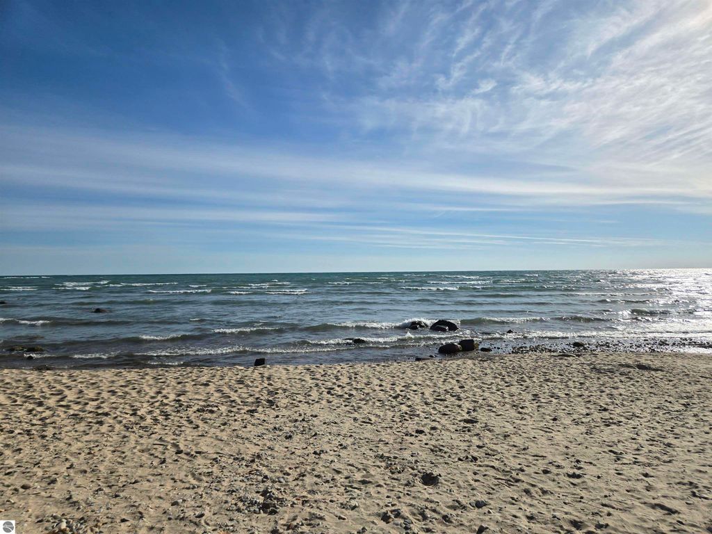 Scenic view of Lake Huron shoreline with sandy beach, gentle waves, and clear blue sky, highlighting proximity to public access for property at 5971 E Point Road, Harrisville, MI.