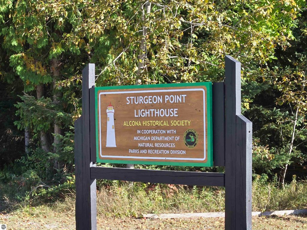 Sturgeon Point Lighthouse sign with surrounding trees, highlighting its historical significance and location near Lake Huron in Harrisville, MI.