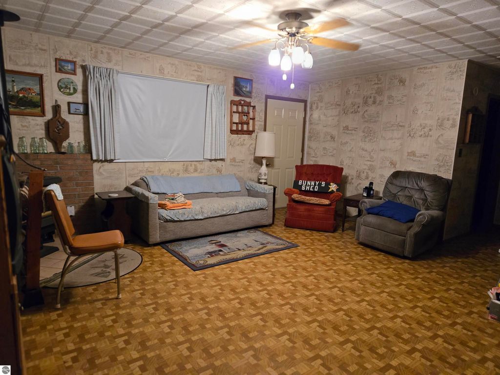 Cozy living room featuring a blue sofa, red armchair with "BUNNY'S SHED" sign, and wooden decor, showcasing a warm, inviting atmosphere in the 2-bedroom home at 5971 E Point Road, Harrisville, MI.