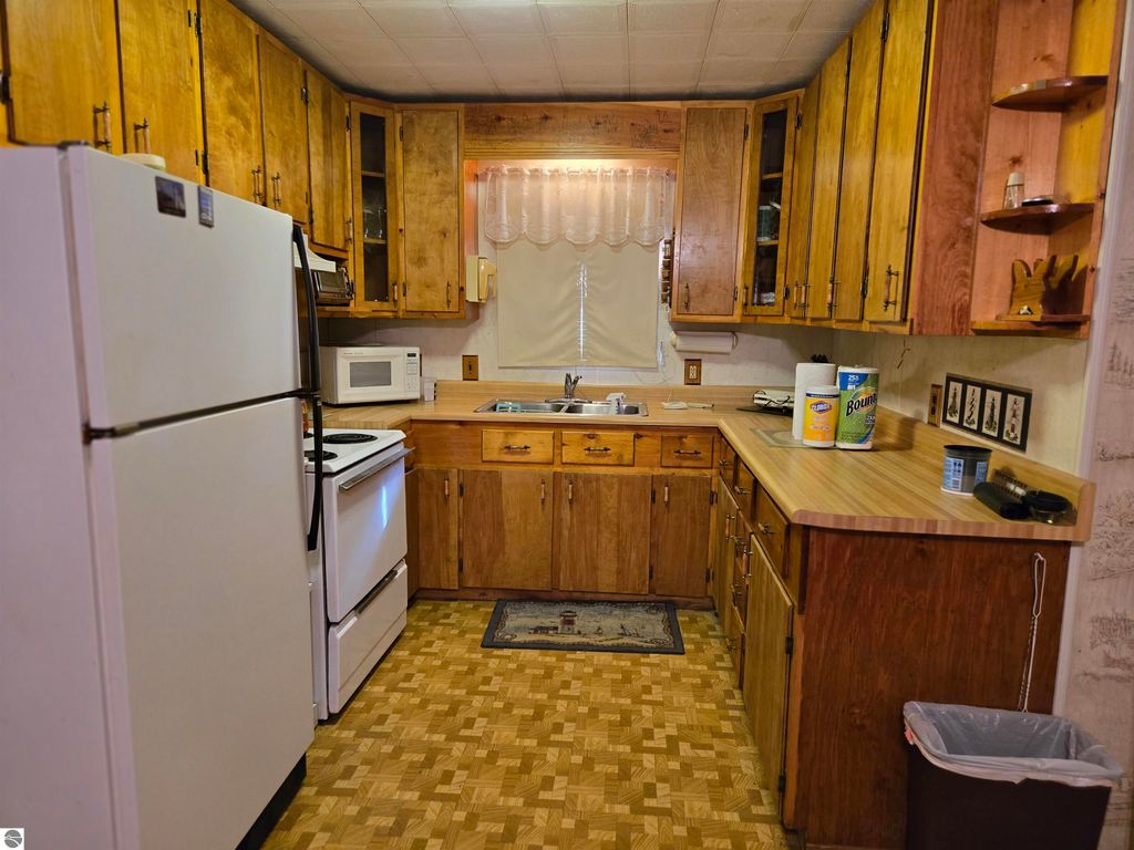 Cozy kitchen featuring wooden cabinetry, white appliances including refrigerator and oven, and a countertop with a sink, ideal for a 2-bedroom home in Harrisville, MI.