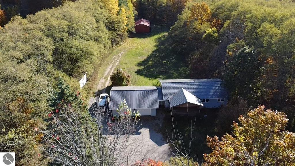 Aerial view of ranch-style home at 8721 Glover Lake Road, Bear Lake, MI, showcasing 3 bedrooms, 2 baths, large yard on 4.68 acres, with a red pole barn and surrounded by trees.