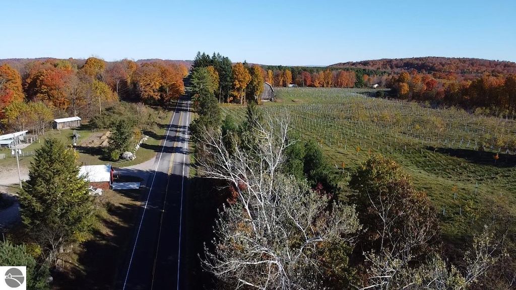 Aerial view of 8721 Glover Lake Road, Bear Lake, MI, showcasing colorful autumn foliage, nearby road, and expansive fields, highlighting the property's rural setting and proximity to nature.
