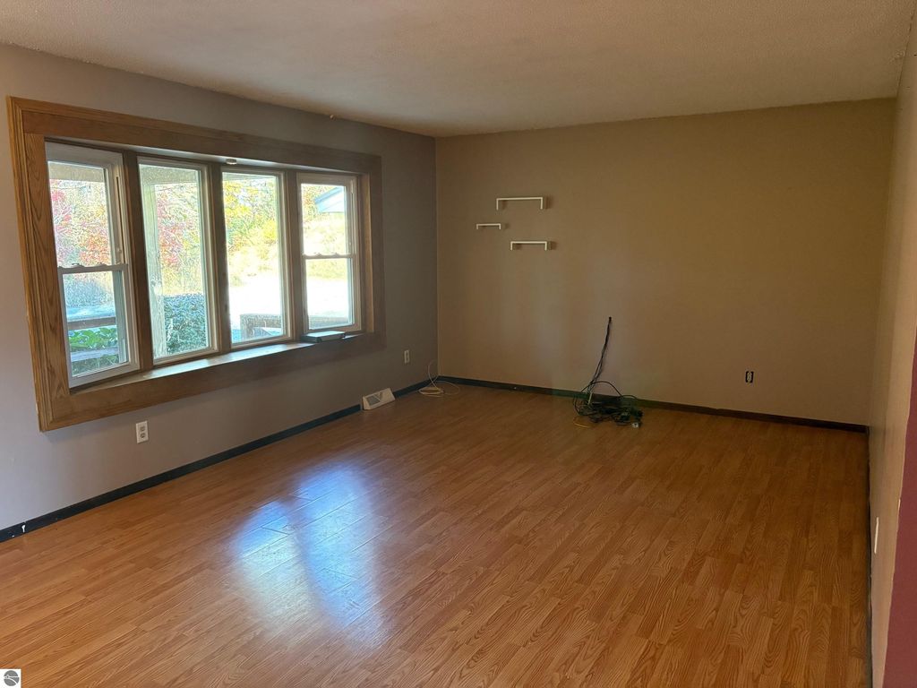 Interior view of a ranch-style home living room with large bay window, hardwood flooring, and neutral wall colors, showcasing spacious layout ideal for family living near Bear Lake, MI.