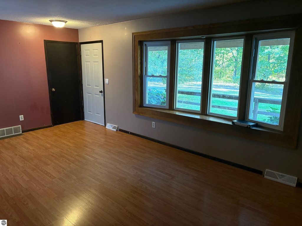 Interior view of a ranch-style home living room featuring hardwood flooring, a large bay window with natural light, and doors leading to adjacent rooms, highlighting the spacious layout near Bear Lake, MI.