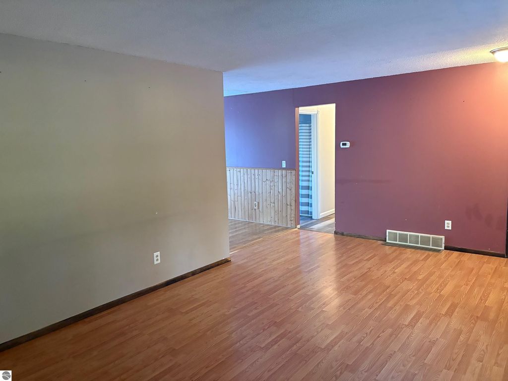 Interior view of a ranch-style home featuring hardwood floors, a neutral wall color, and an open layout leading to a doorway, reflecting the living space of the property at 8721 Glover Lake Road, Bear Lake, MI.