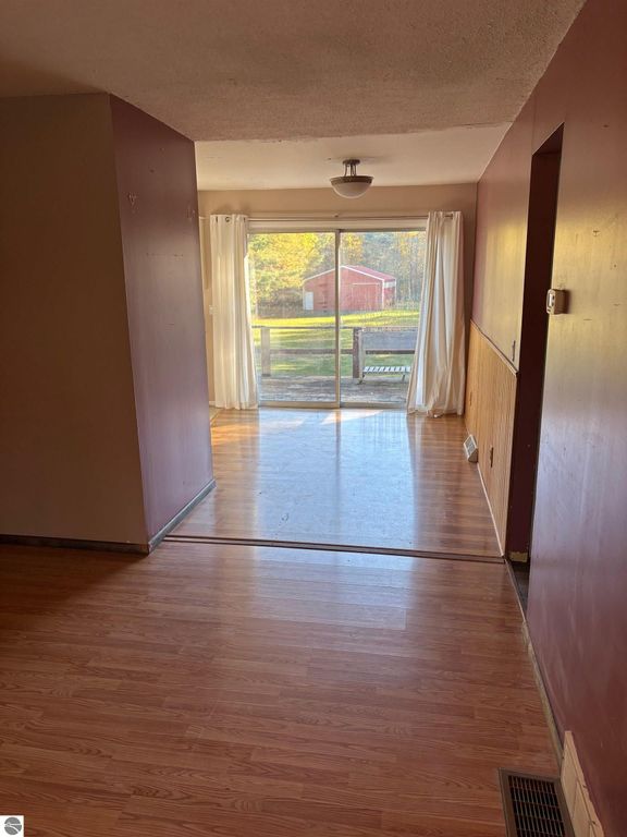 Interior view of ranch-style home showing large living room with hardwood flooring, sliding glass door leading to backyard, and natural light from windows, highlighting nearby red barn.