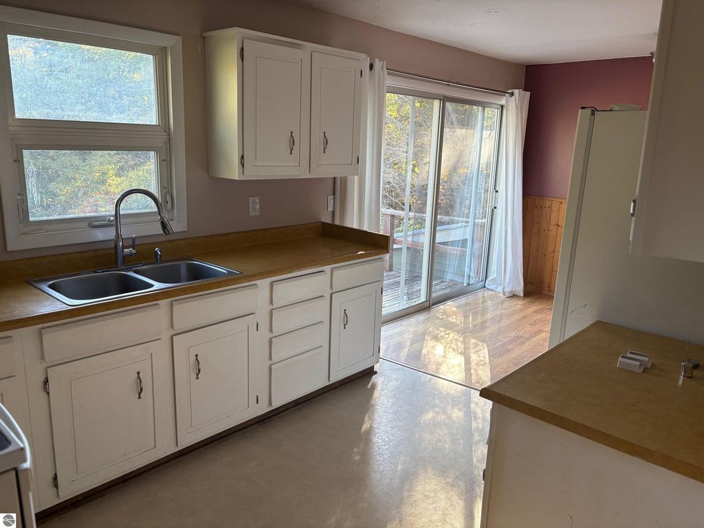 Kitchen interior of ranch-style home at 8721 Glover Lake Road, featuring white cabinetry, double sink, and sliding glass door leading to outdoor deck.