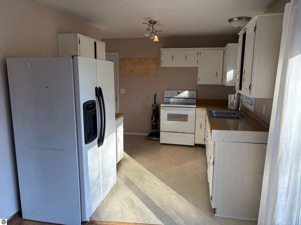 Kitchen interior featuring white appliances, including a refrigerator and stove, with wooden countertops and light-colored cabinetry, showcasing a spacious layout in a ranch-style home at 8721 Glover Lake Road, Bear Lake, MI.