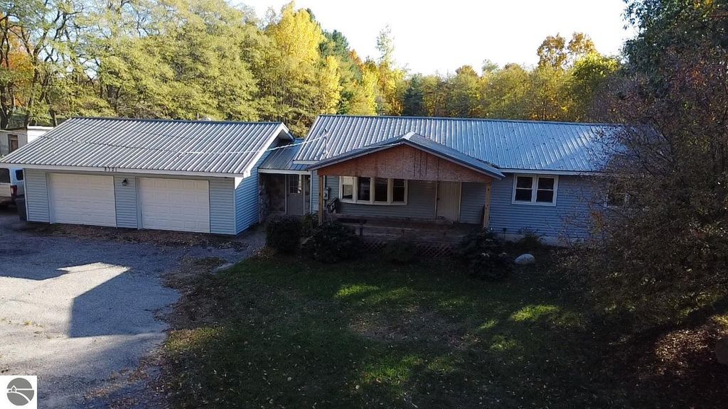 Ranch-style home at 8721 Glover Lake Road, Bear Lake, MI, featuring a new steel roof, attached two-car garage, and surrounded by trees on nearly 5 acres.
