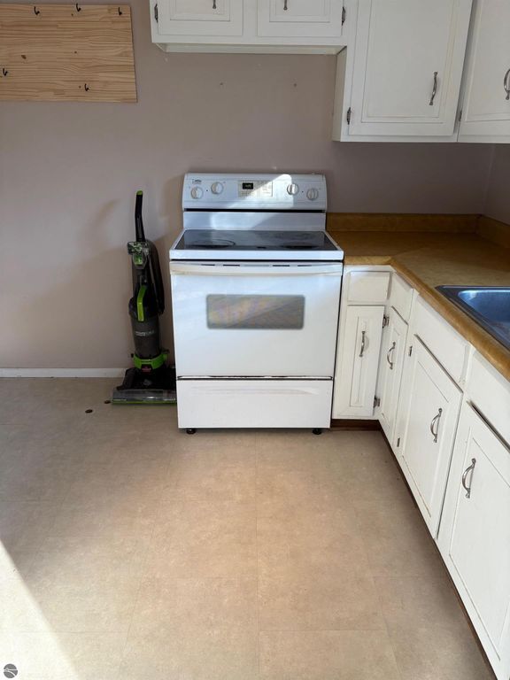 Kitchen featuring a white stove, countertop, and sink, with a vacuum cleaner in the corner, showcasing the interior of the ranch-style home for sale at 8721 Glover Lake Road, Bear Lake, MI.
