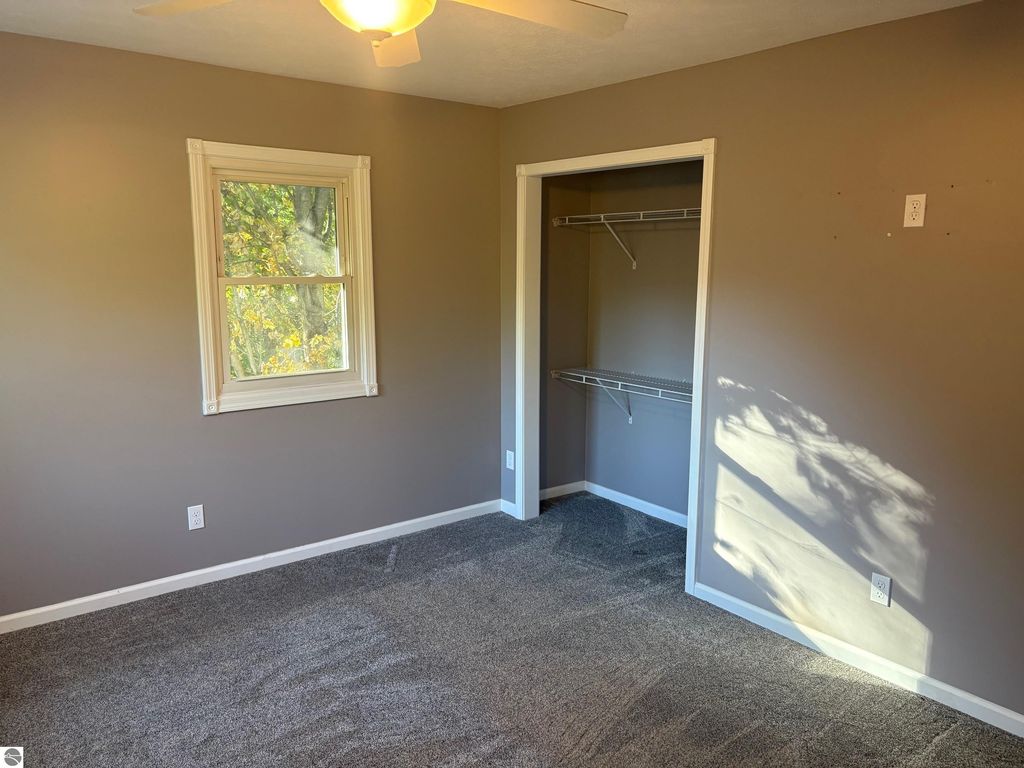Bedroom with gray walls, window providing natural light, and a closet with shelving, showcasing spacious interior of the Bear Lake property listing at 8721 Glover Lake Road.