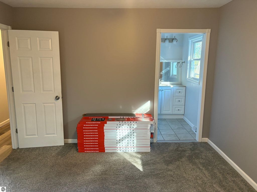 Interior view of a room featuring a stack of flooring materials, a closed door, and an adjacent bathroom area with white cabinetry and tile flooring, highlighting recent renovations in the ranch-style home at 8721 Glover Lake Road, Bear Lake, MI.
