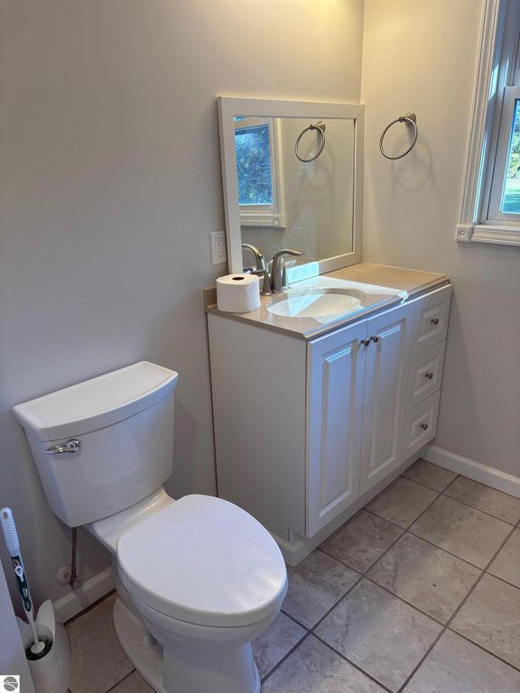 Modern bathroom featuring a toilet, sink with countertop, and mirror, showcasing clean lines and neutral colors, ideal for a ranch-style home in Bear Lake, MI.