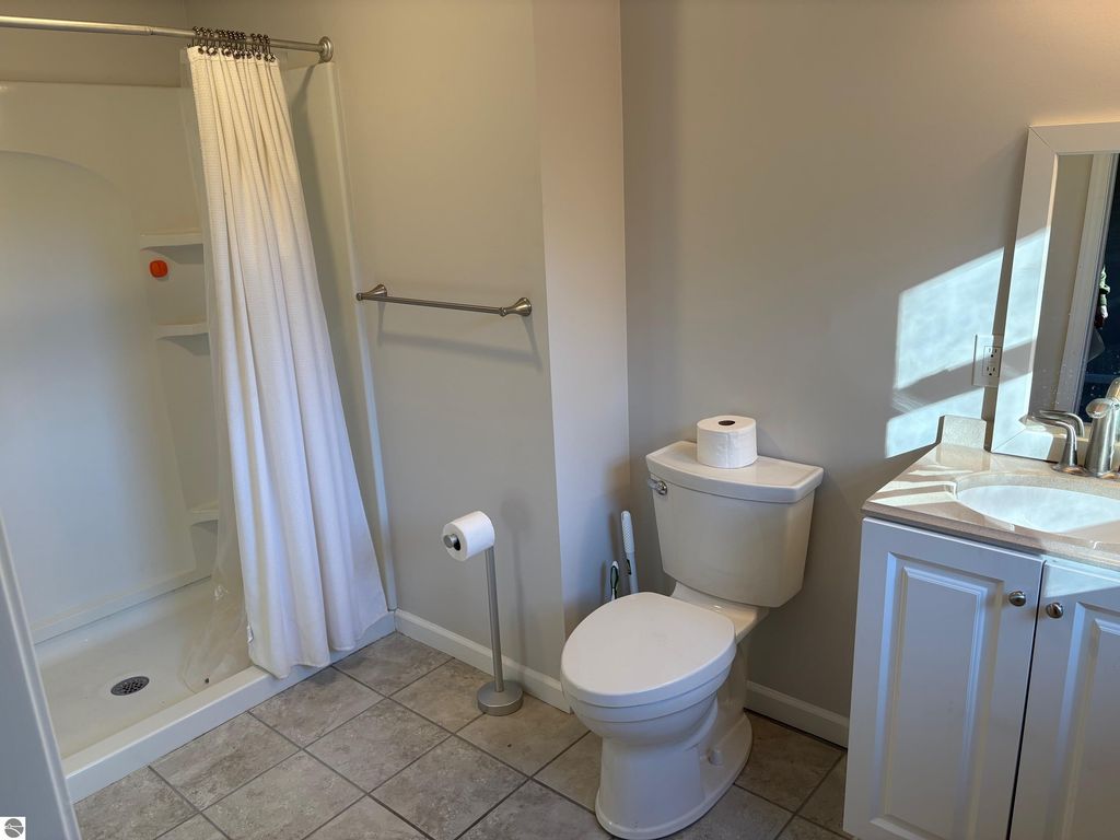 Bathroom featuring a shower with a white curtain, toilet, and vanity with sink, showcasing clean tiles and modern fixtures in a well-lit space.