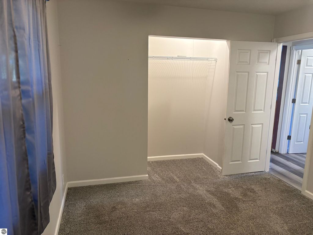 Interior view of a bedroom featuring beige walls, gray carpet, and a closet with wire shelving, showcasing the room's spaciousness and natural light.