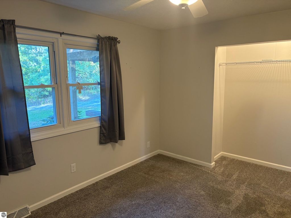 Bedroom interior featuring windows with gray curtains, carpeted floor, ceiling fan, and a closet space, part of the ranch-style home for sale at 8721 Glover Lake Road, Bear Lake, MI.