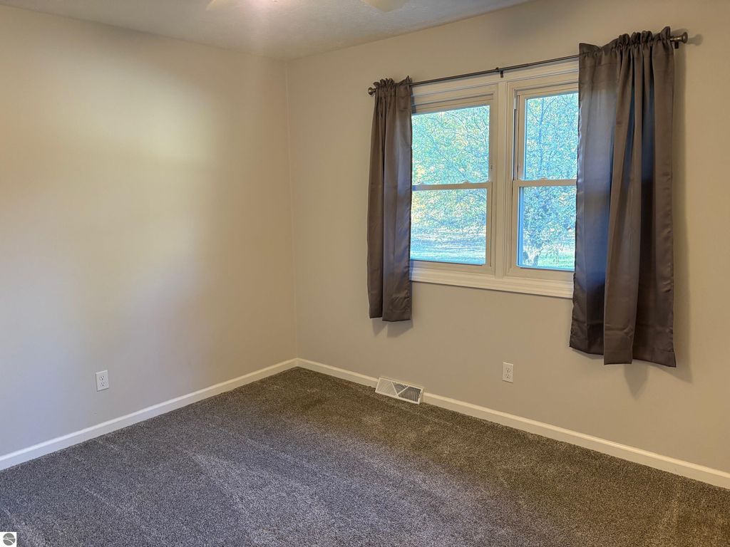 Cozy bedroom featuring gray carpet, neutral walls, large windows with dark curtains, and natural light illuminating the space, part of the 3 bed, 2 bath ranch-style home at 8721 Glover Lake Road, Bear Lake, MI.