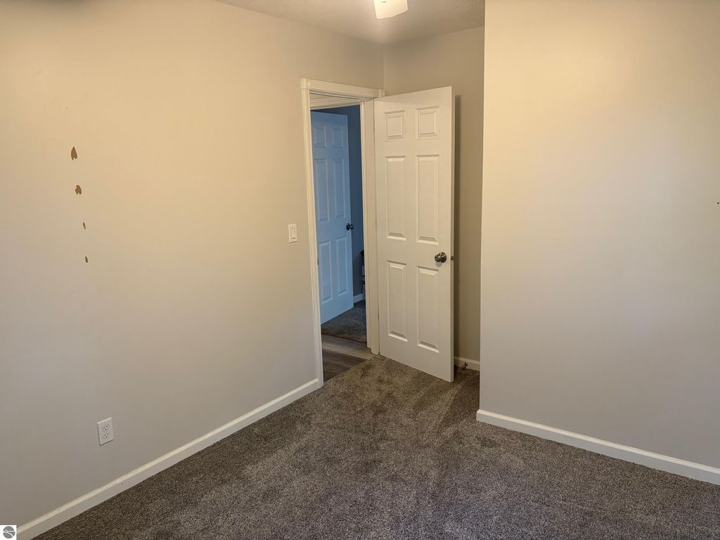 Interior view of a bedroom featuring a light-colored wall, carpeted floor, and open door leading to another room, showcasing the home's layout at 8721 Glover Lake Road, Bear Lake, MI.