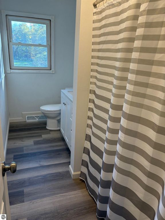 Bathroom interior featuring a striped shower curtain, toilet, and vanity, with natural light from a window and modern flooring.