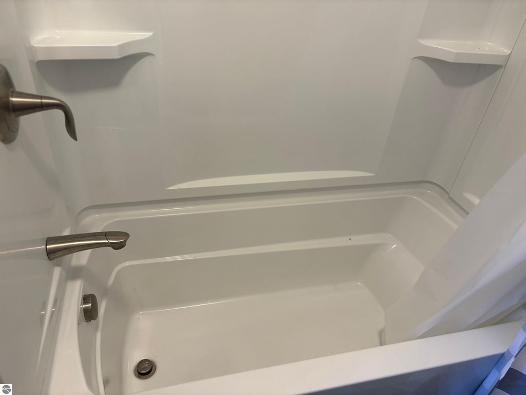 Modern bathtub and shower enclosure with chrome fixtures, featuring a clean, white surface and built-in shelves.