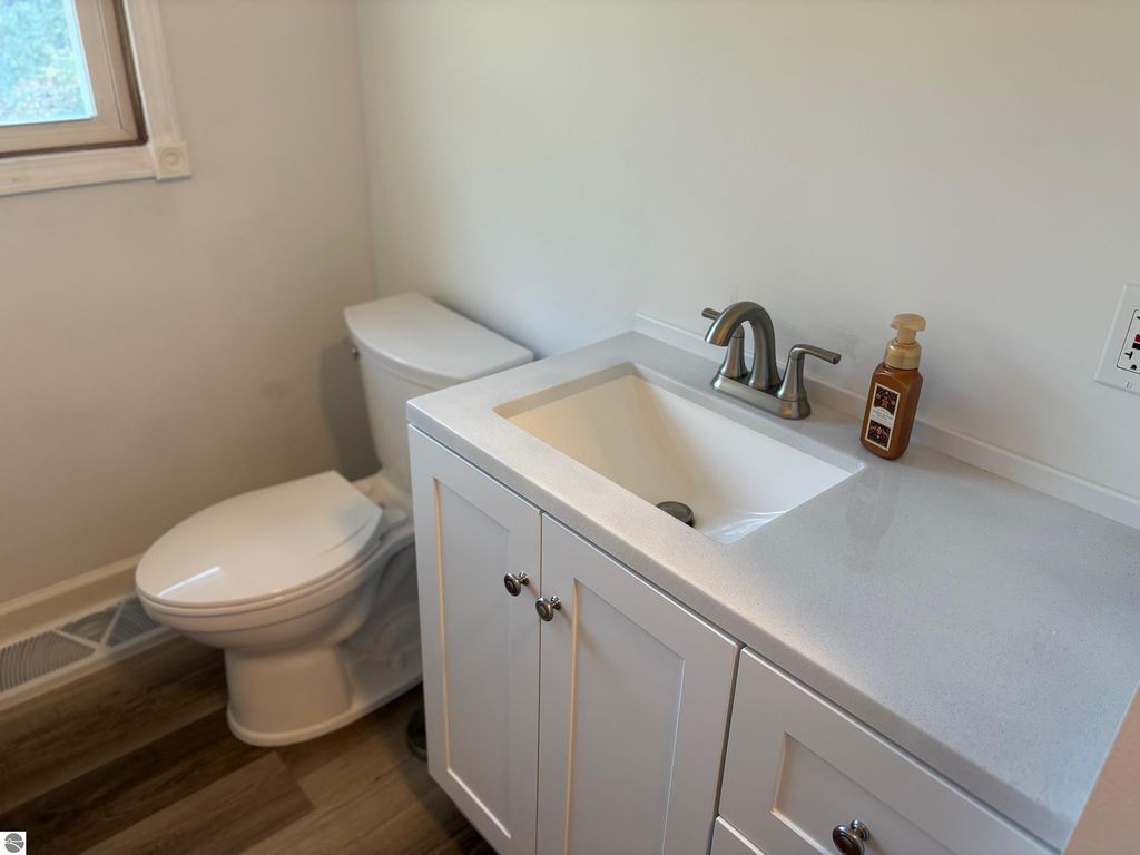 Modern bathroom featuring a white vanity with a sink, a toilet, and a window, showcasing contemporary design elements and natural light.