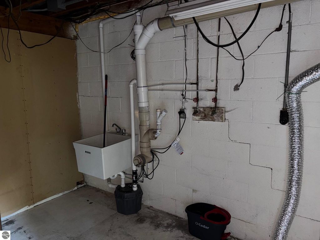 Basement utility area featuring a laundry sink, plumbing pipes, and drainage system, relevant to the 3-bedroom ranch-style home at 8721 Glover Lake Road, Bear Lake, MI.