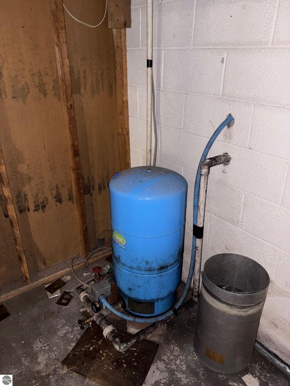 Water pressure tank in basement, blue cylindrical tank with connected pipes and a metal container, indicative of plumbing features in Bear Lake home listing.