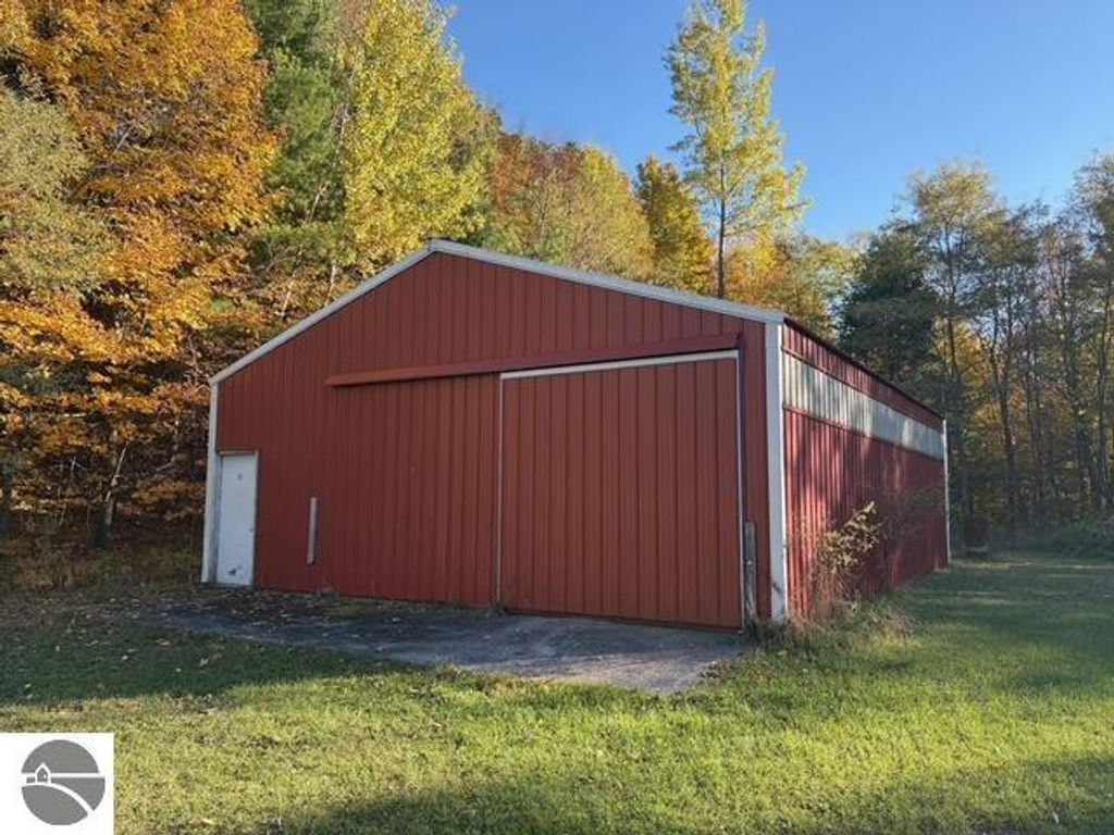 Red pole barn with sliding doors and concrete floor, surrounded by autumn foliage, located on property at 8721 Glover Lake Road, Bear Lake, MI.