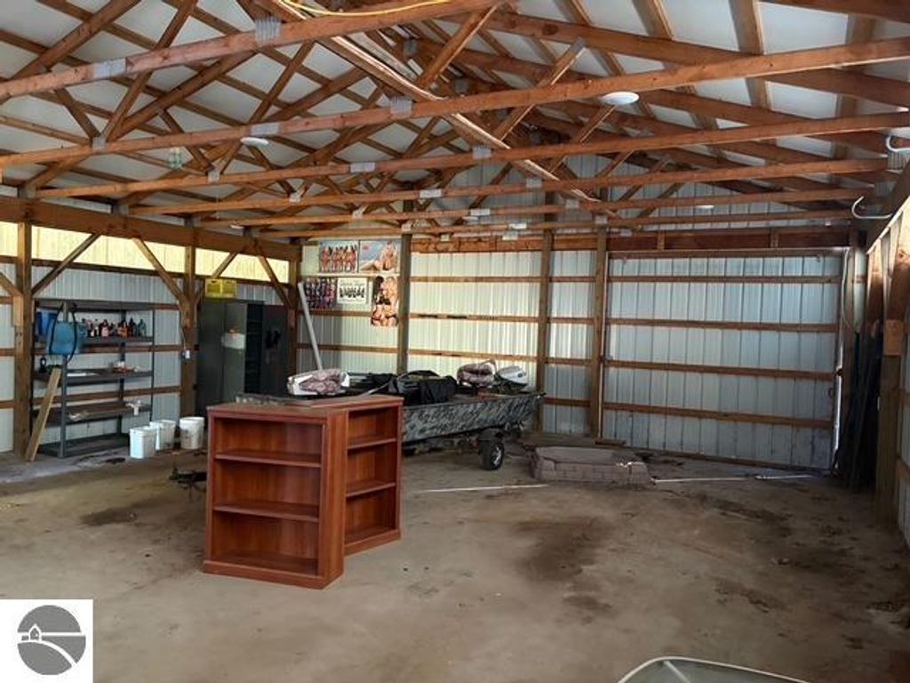 Interior of a 30 x 40 pole barn with wooden beams, concrete floor, shelving, and storage spaces, showcasing potential for workshop or storage use near 8721 Glover Lake Road, Bear Lake, MI.