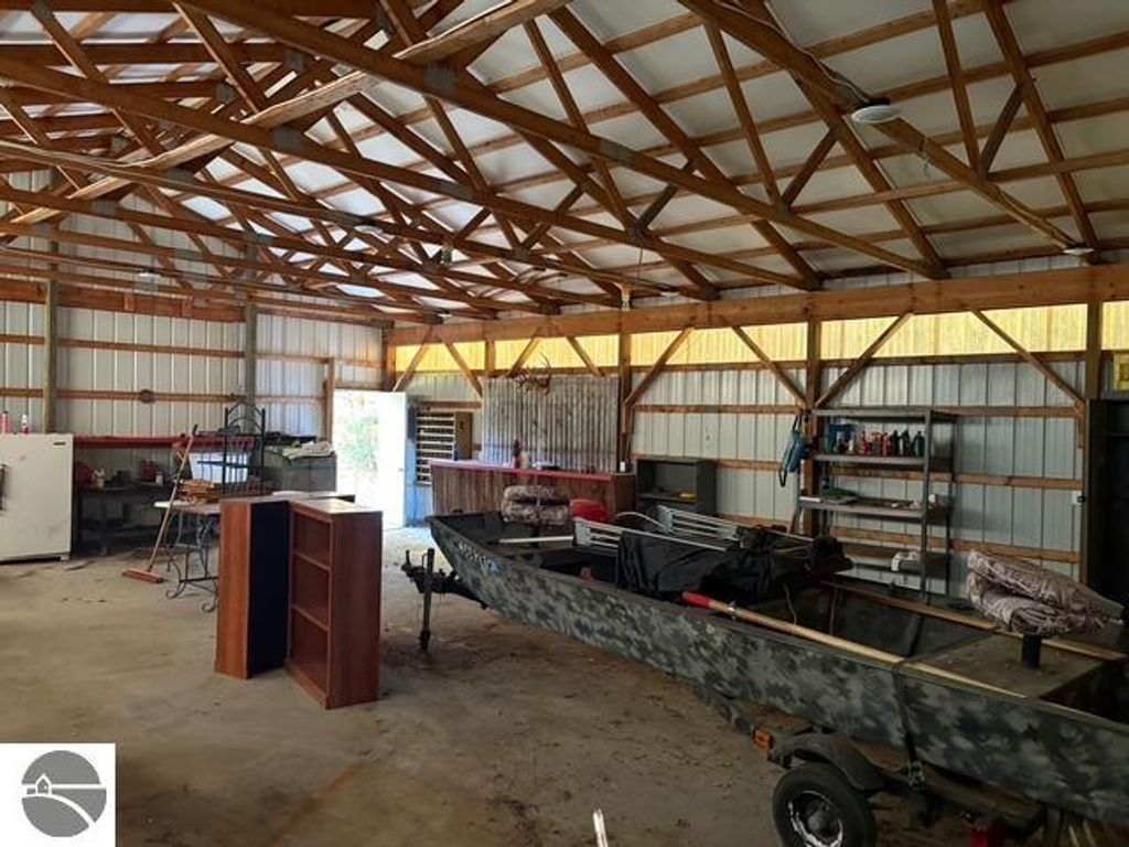 Interior of a spacious pole barn featuring wooden beams, a camouflaged boat, workbench, and storage shelving, highlighting the additional storage options available at 8721 Glover Lake Road, Bear Lake, MI.