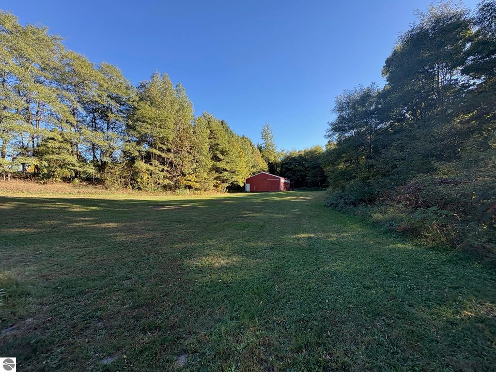 Red barn on a grassy lot surrounded by trees, showcasing the outdoor space of the property at 8721 Glover Lake Road, Bear Lake, MI.
