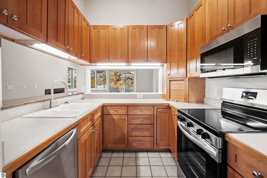 Updated kitchen with wooden cabinetry, modern appliances, and large windows providing natural light, showcasing the condo at 3756 Country Club Drive #9 in Traverse City, MI.