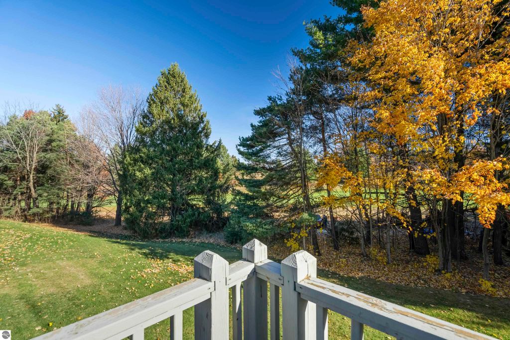 View from the balcony of a condo at 3756 Country Club Drive, showcasing a serene landscape with mature trees and autumn foliage, overlooking a golf course in Traverse City, MI.