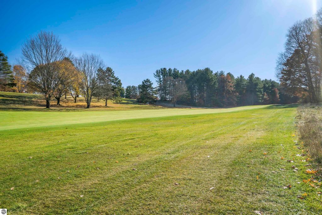 Scenic view of a golf course with lush green grass and mature trees in Traverse City, Michigan, showcasing the tranquil outdoor setting near the condo at 3756 Country Club Drive #9.