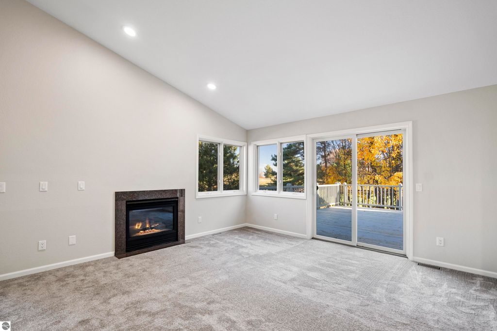 Light-filled living room in a 2-bedroom condo featuring a cozy gas fireplace, large windows overlooking a deck, and fresh updates in a peaceful setting near a golf course in Traverse City, MI.