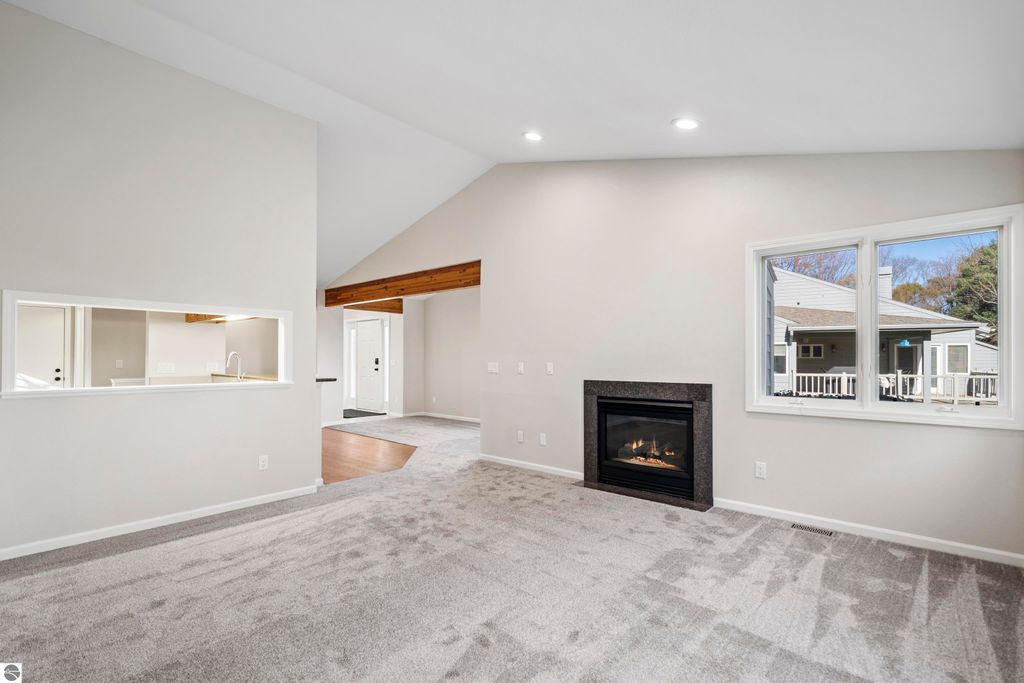 Light-filled living room with vaulted ceilings, cozy gas fireplace, and large windows overlooking a private balcony in a Traverse City condo.