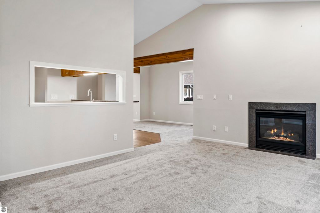 Light-filled living room in a 2-bedroom condo, featuring vaulted ceilings, cozy gas fireplace, and a view towards the kitchen with a serving window, showcasing fresh updates and a spacious layout.