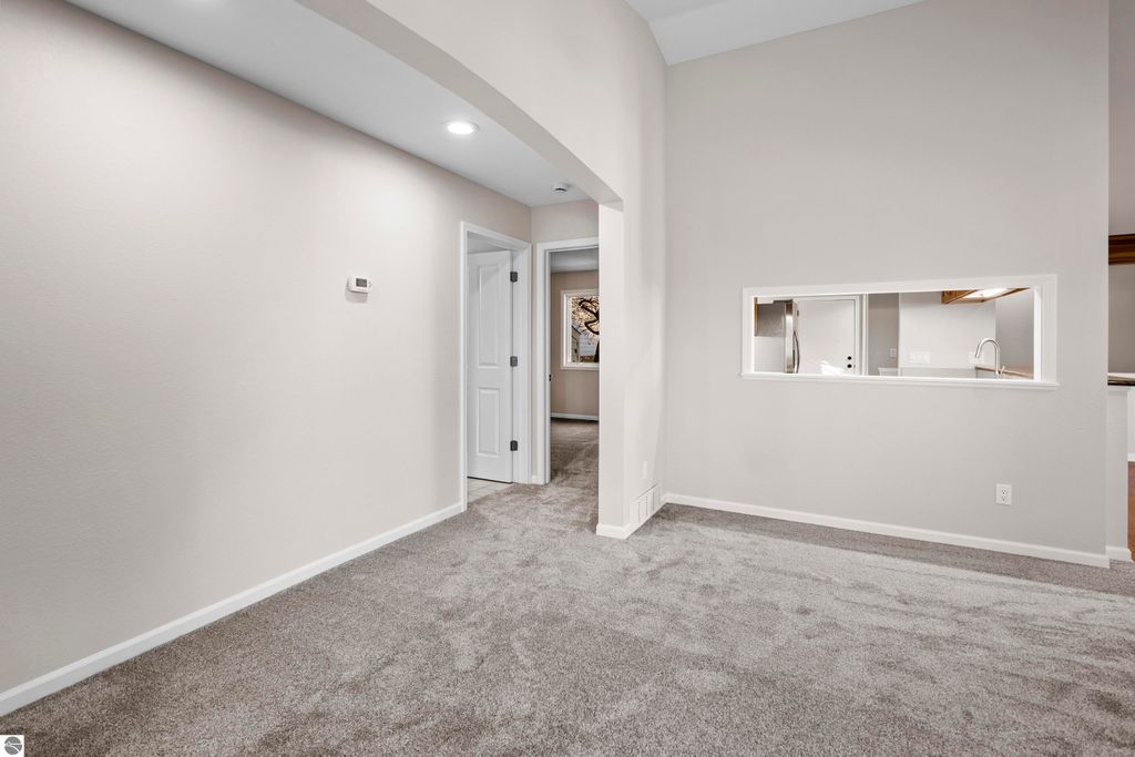 Updated interior of a 2-bedroom condo in Traverse City, featuring light-colored walls, plush carpeting, and an open layout with a view into the kitchen area through a serving window.