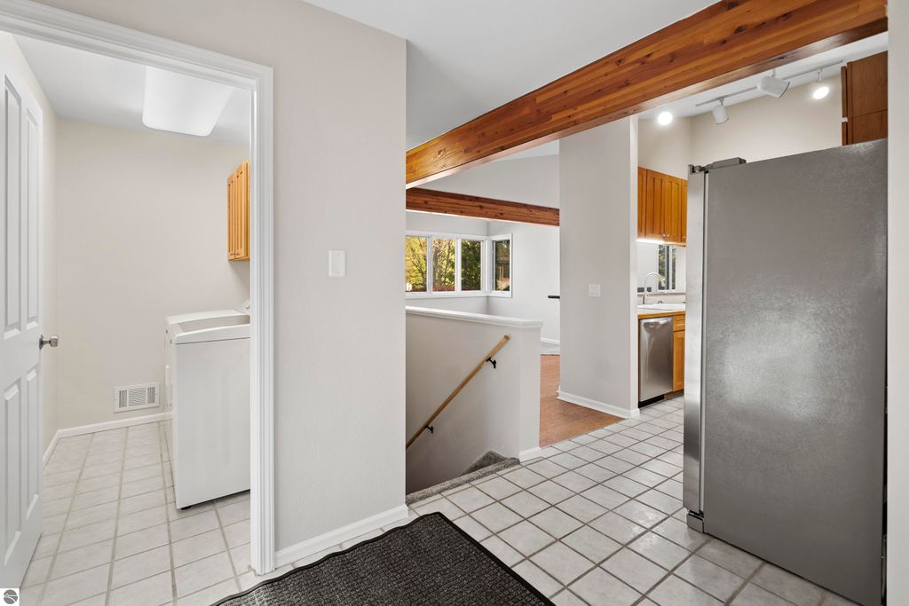 Updated kitchen and laundry area in a 2-bedroom condo, featuring light-colored walls, tile flooring, wooden cabinetry, and a stainless steel refrigerator, situated in Traverse City, MI.