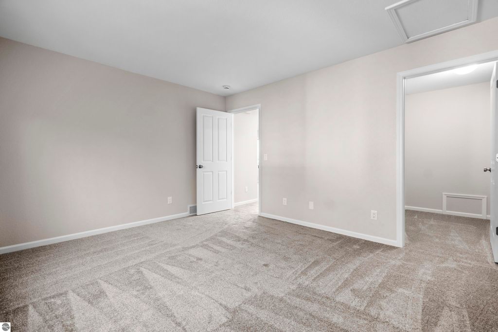 Light-filled, freshly updated interior of a 2-bedroom condo in Traverse City, featuring new carpeting, neutral wall colors, and open doorways leading to additional rooms.