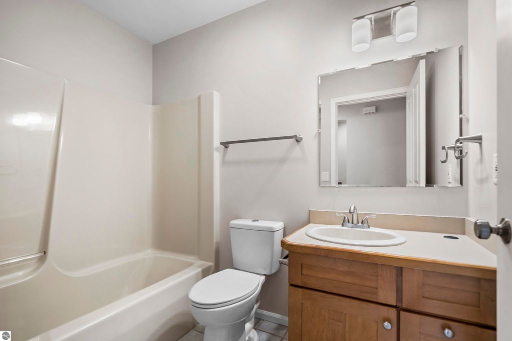 Updated bathroom featuring a shower/tub combo, toilet, and sink with wooden cabinetry in a condo at 3756 Country Club Drive, Traverse City, MI.