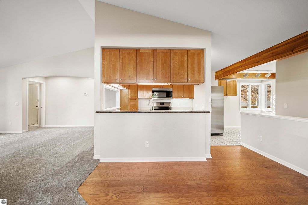 Updated kitchen and living area of a 2-bedroom condo in Traverse City, featuring wood cabinets, stainless steel appliances, and open layout with vaulted ceilings and new carpeting.