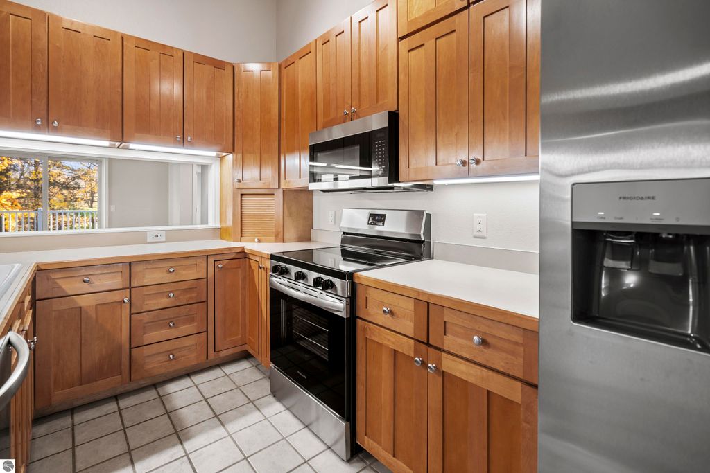 Updated kitchen with wooden cabinetry, stainless steel appliances, and a window overlooking outdoor scenery in a Traverse City condo.