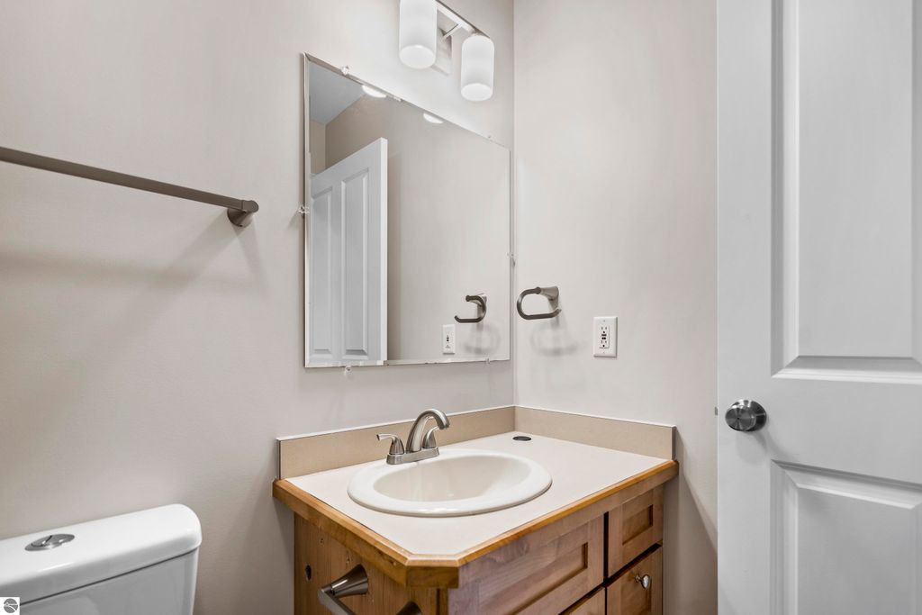 Updated bathroom with a wooden vanity, round sink, and modern lighting fixtures, featuring a large mirror and neutral wall colors, located in a 2-bedroom condo in Traverse City, MI.