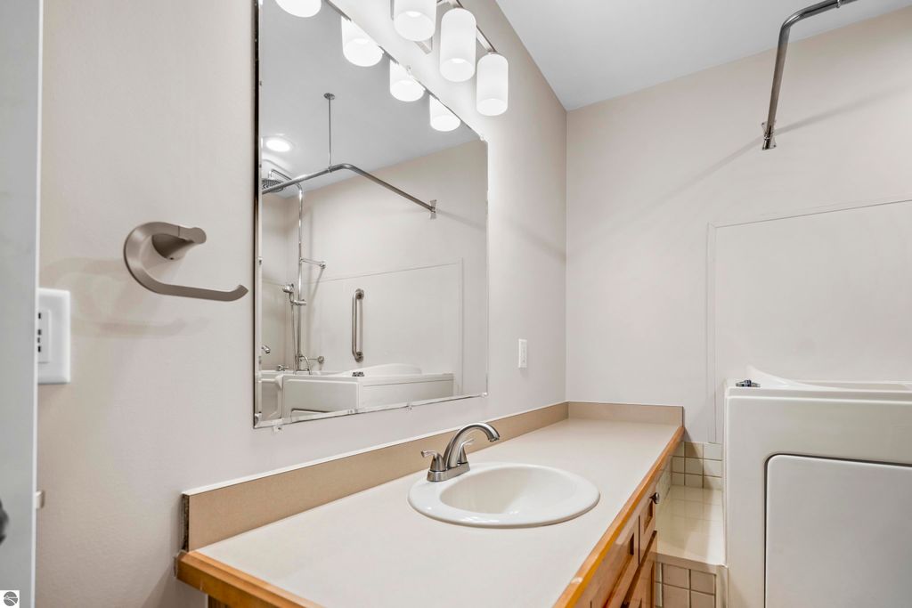 Updated bathroom with modern lighting, sink, and laundry appliances in a 2-bedroom condo at 3756 Country Club Drive, Traverse City, MI.