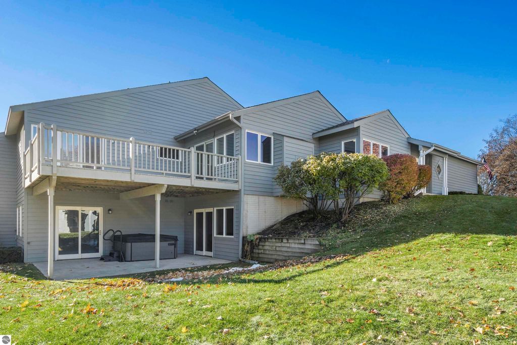 Exterior view of a 2-bedroom, 2-bath condo at 3756 Country Club Drive #9 in Traverse City, featuring a spacious deck, patio area, and landscaped surroundings with mature trees, showcasing the peaceful setting adjacent to a golf course.